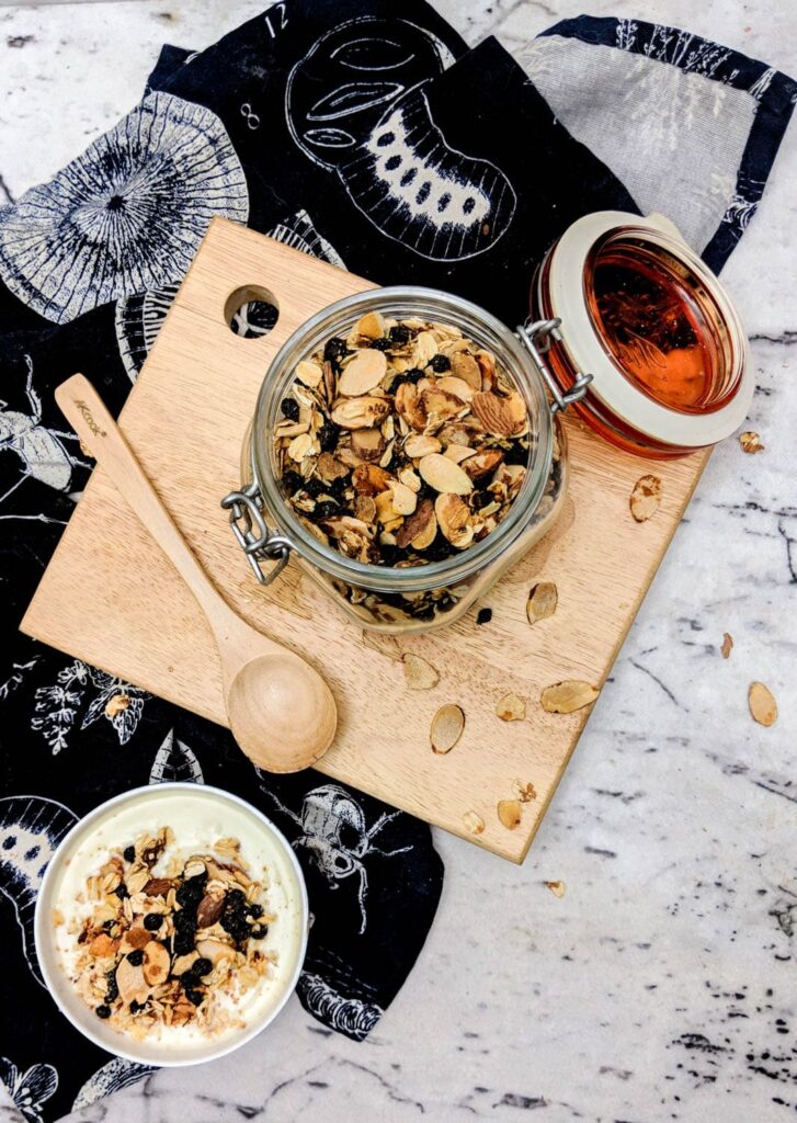 Top view of a storage jar of gluten free granola as well as a bowl of gluten free granola served over yogurt.