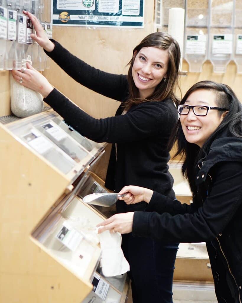 Kathryn and a friend demonstrating how to be conscious consumer by shopping from bulk bins using reusable bags and containers.
