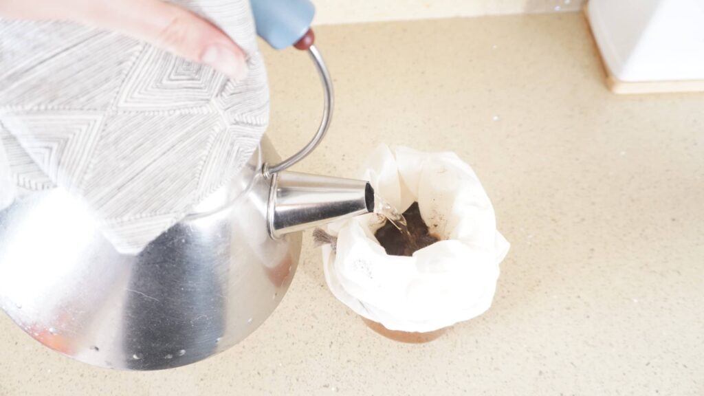 Tea being made by pouring hot water over loose leaf tea in a nut milk bag over a mug.