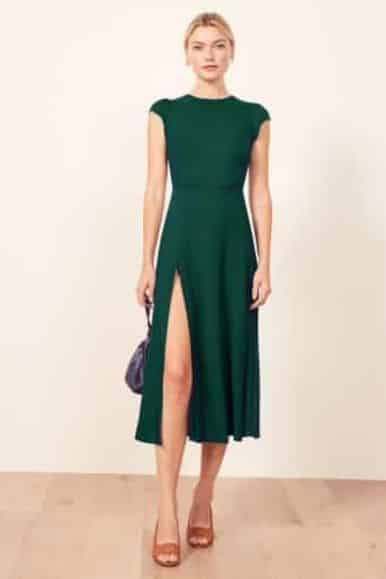 Sustainable cocktail dresses: a woman wearing a a green, high slit dress.